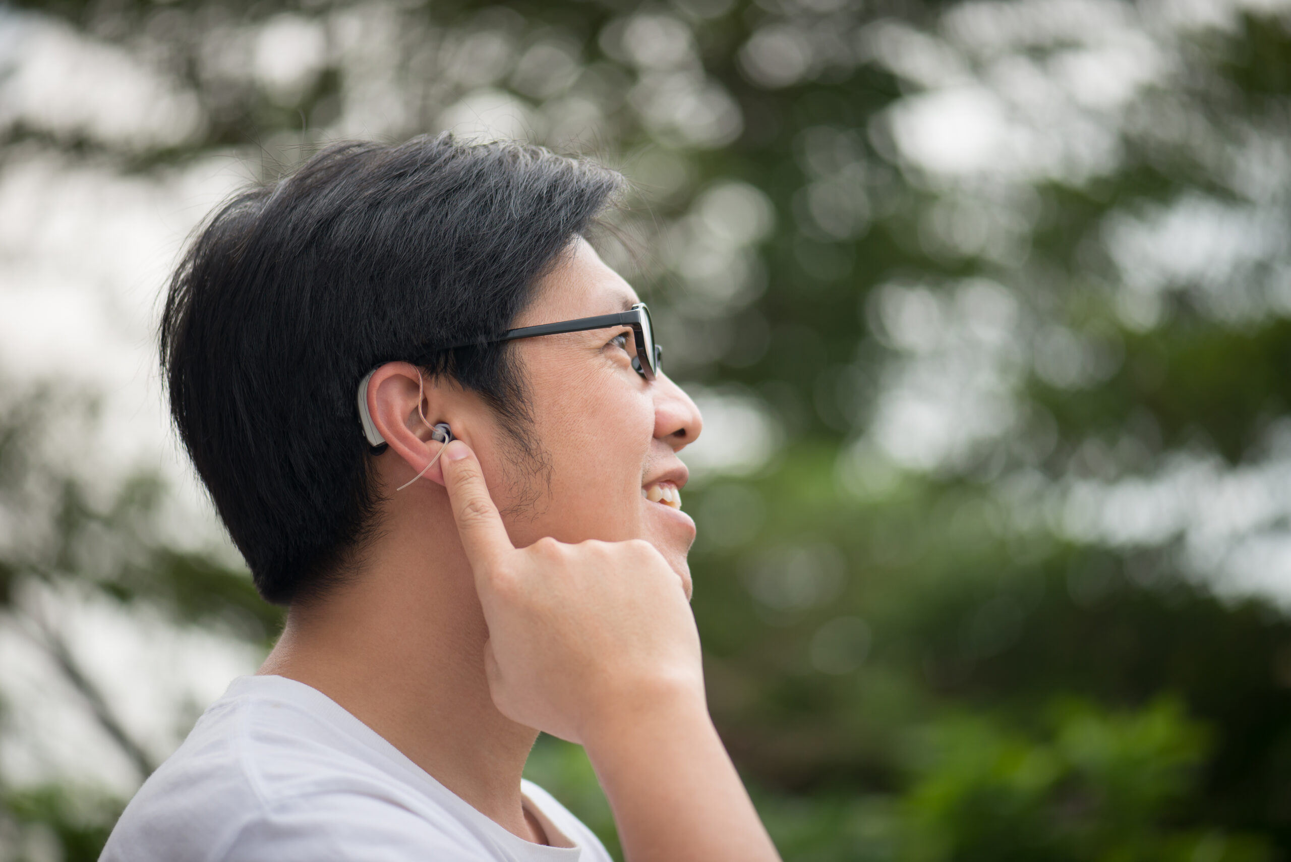 Asian man with hearing aid behind the ear outdoors.